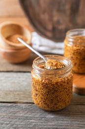 Photo of Jars and spoon of whole grain mustard on wooden table