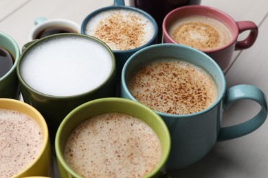 Photo of Many different cups with aromatic hot coffee on white wooden table, closeup