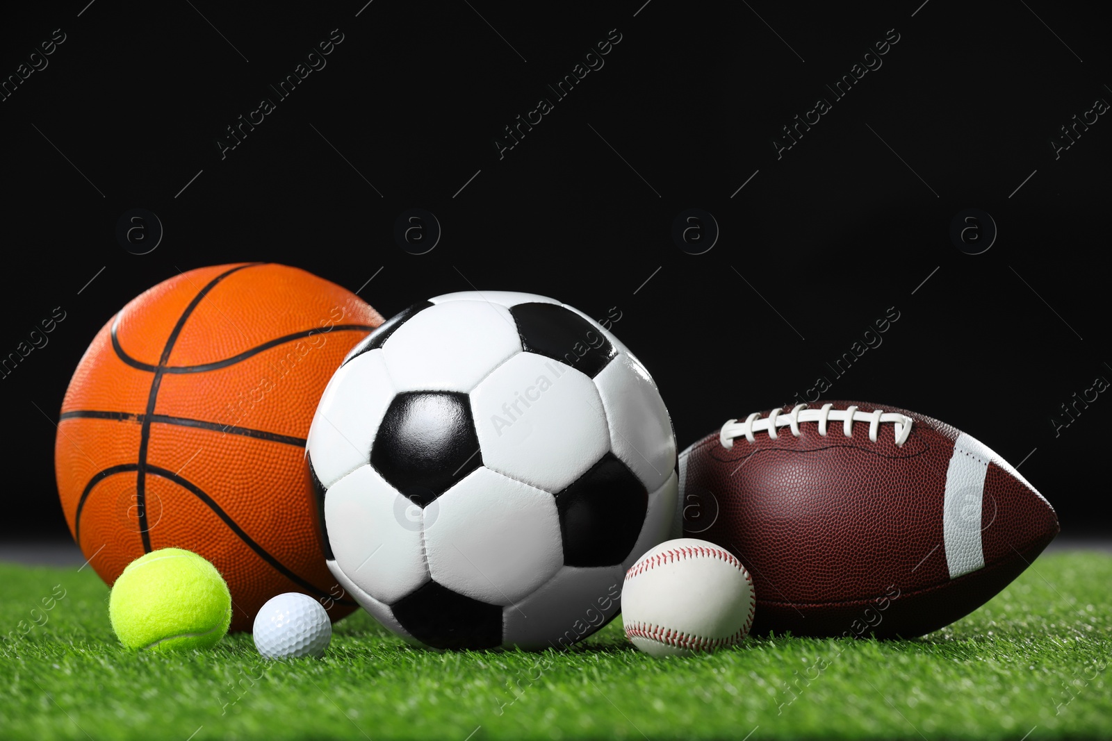 Photo of Many different sports balls on green grass against black background