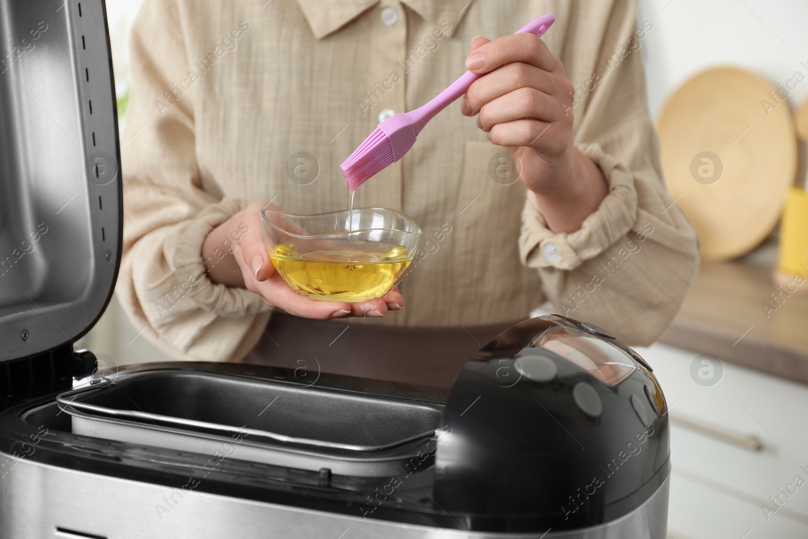 Photo of Woman with oil near breadmaker in kitchen, closeup