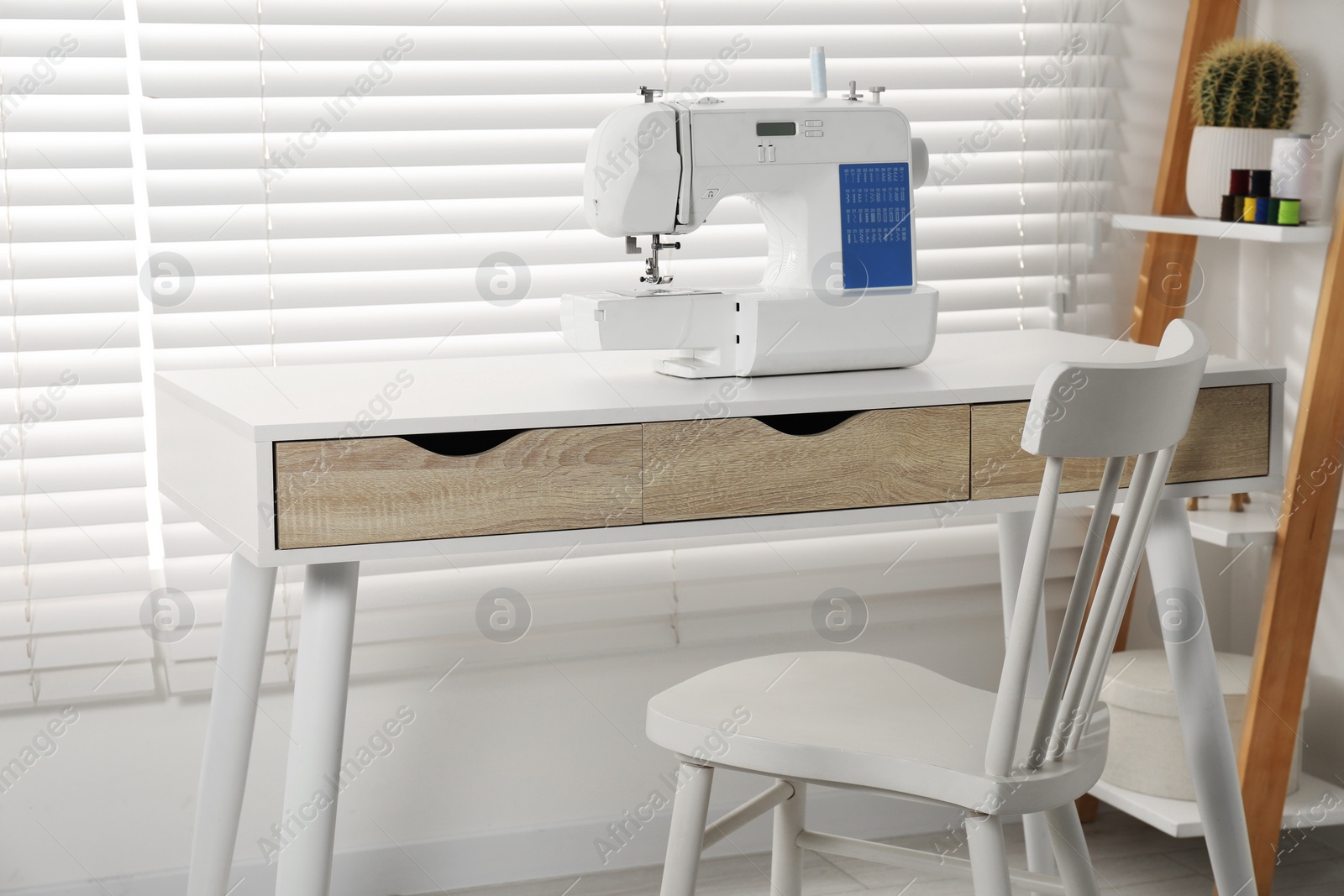 Photo of White sewing machine on wooden desk near chair indoors