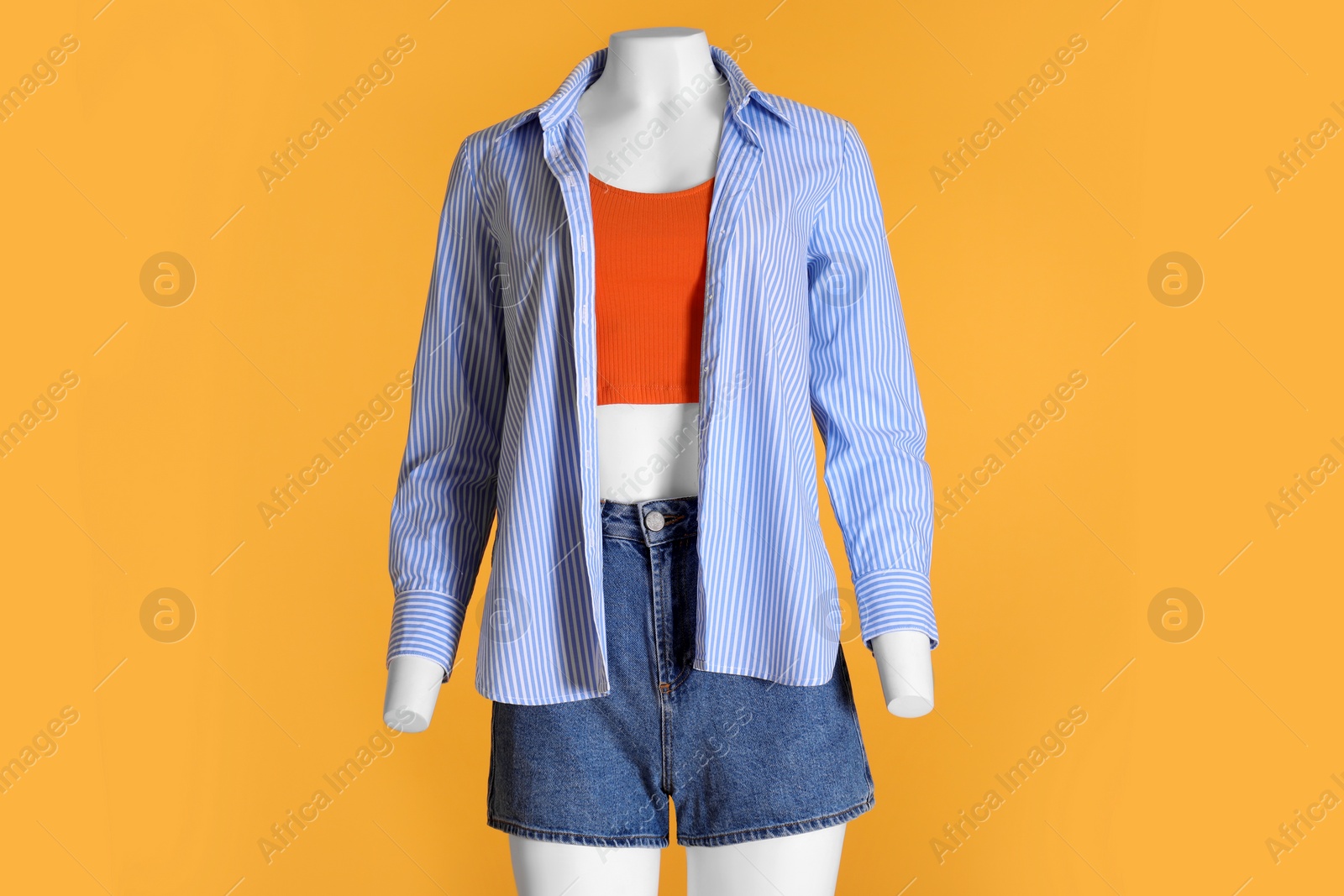 Photo of Female mannequin dressed in tank top, striped shirt and denim shorts on orange background. Stylish outfit