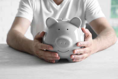 Photo of Man with piggy bank at white table, closeup