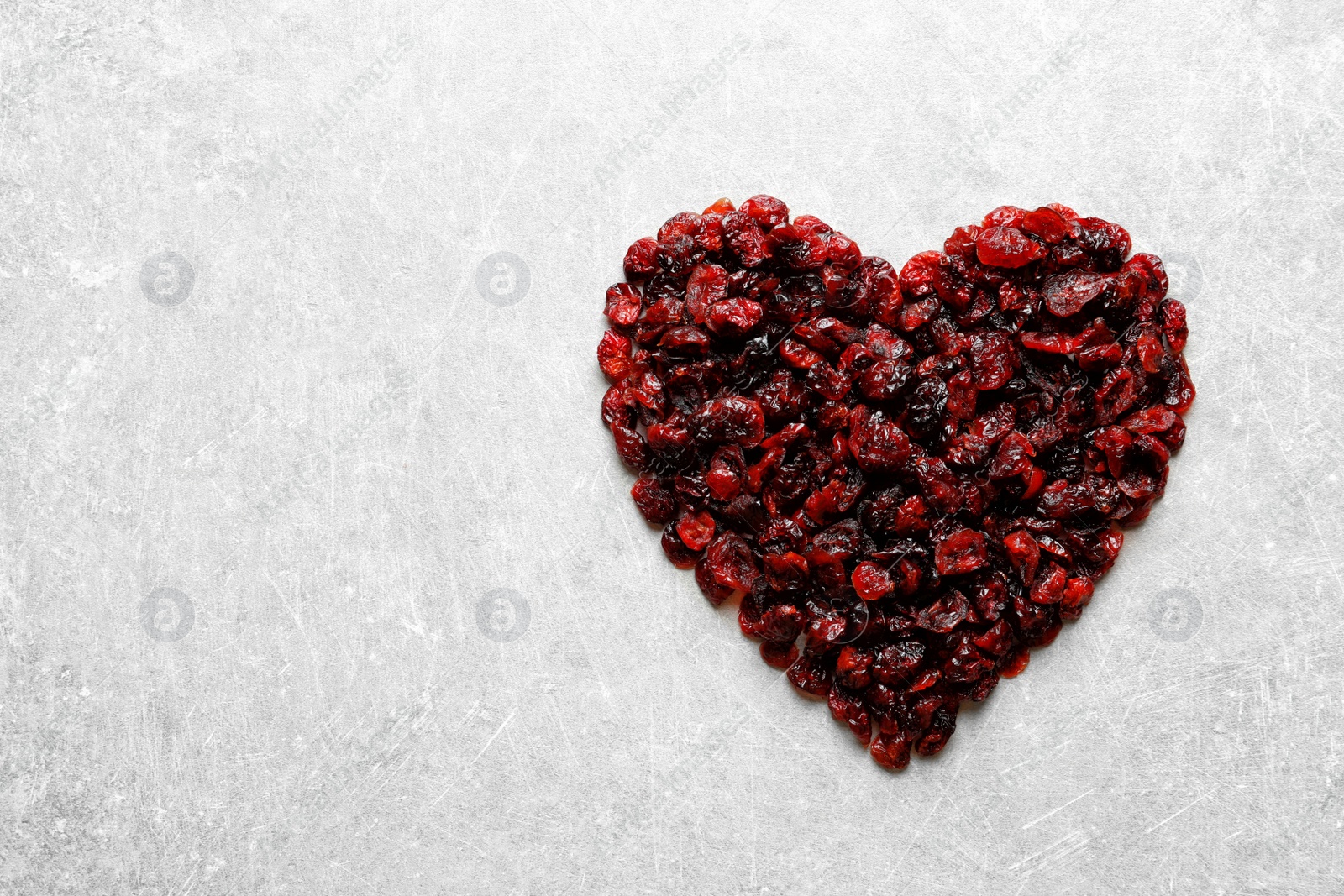 Photo of Heart shaped heap of sweet cranberries on color background, top view with space for text. Dried fruit as healthy snack