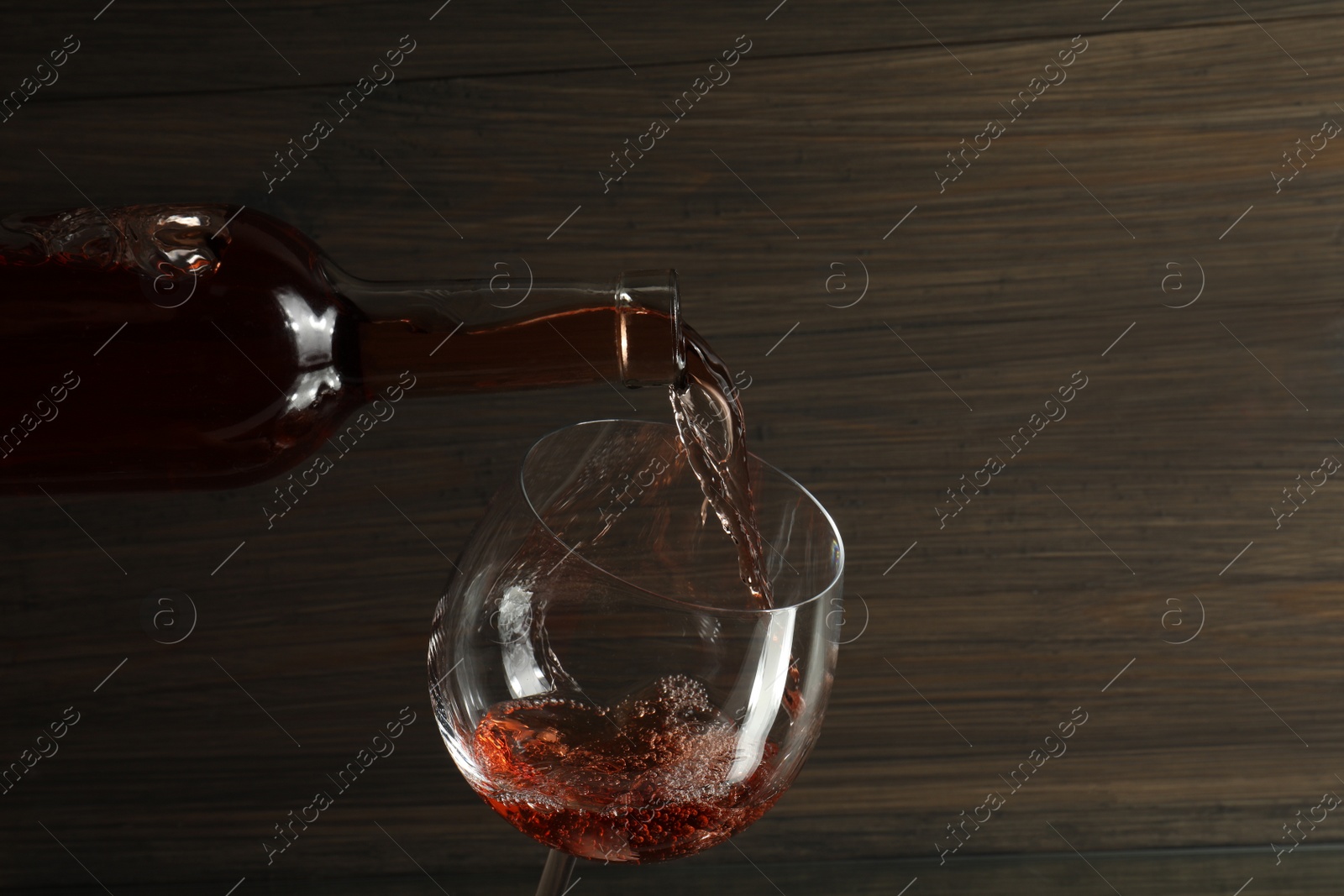 Photo of Pouring rose wine from bottle into glass against wooden background