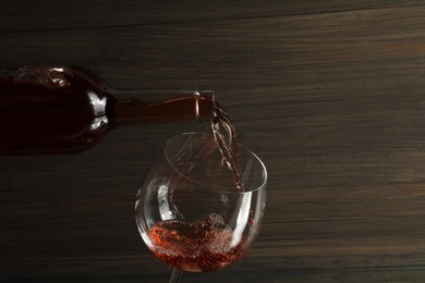 Photo of Pouring rose wine from bottle into glass against wooden background