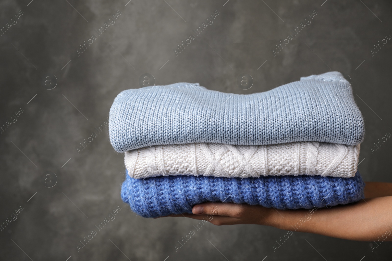 Photo of Woman holding stack of folded warm knitted sweaters against dark background