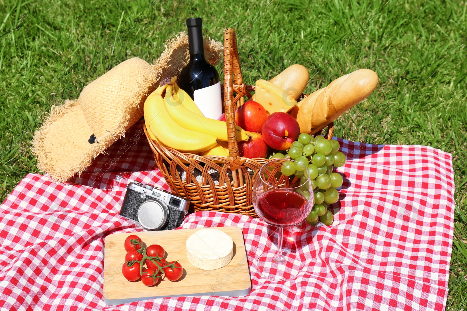 Photo of Basket with food and glass of wine on blanket prepared for picnic in park