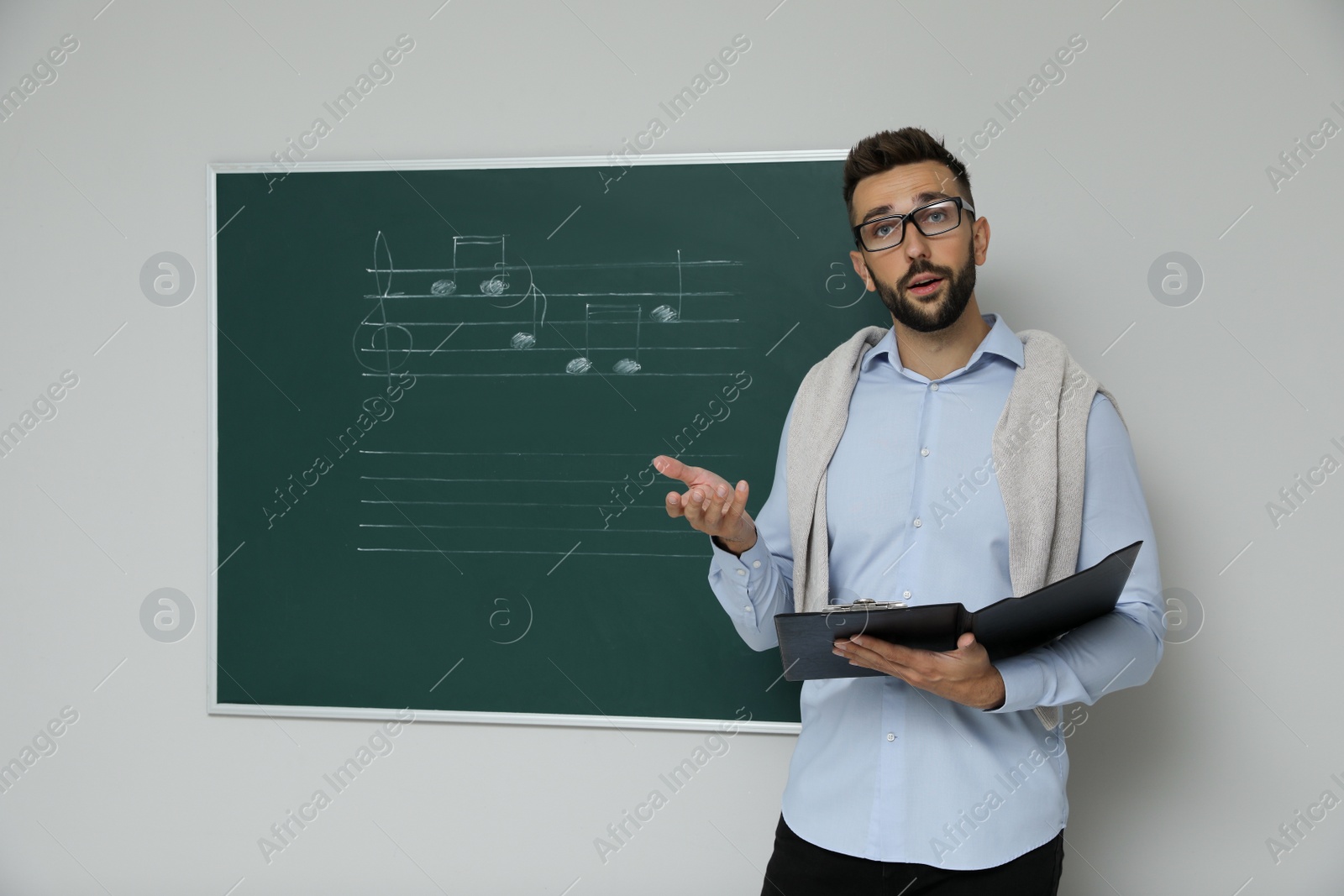 Photo of Teacher near green chalkboard with music notes in classroom