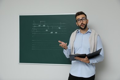 Teacher near green chalkboard with music notes in classroom