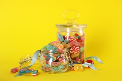 Photo of Jars with different delicious candies on yellow background
