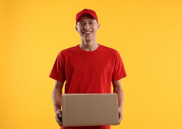 Photo of Happy courier with parcel on yellow background
