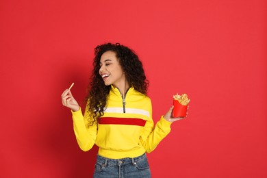 African American woman eating French fries on red background