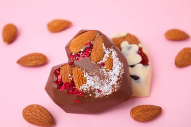 Tasty chocolate heart shaped candies with nuts on pink background, closeup