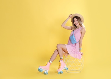 Young woman with retro roller skates on color background, space for text