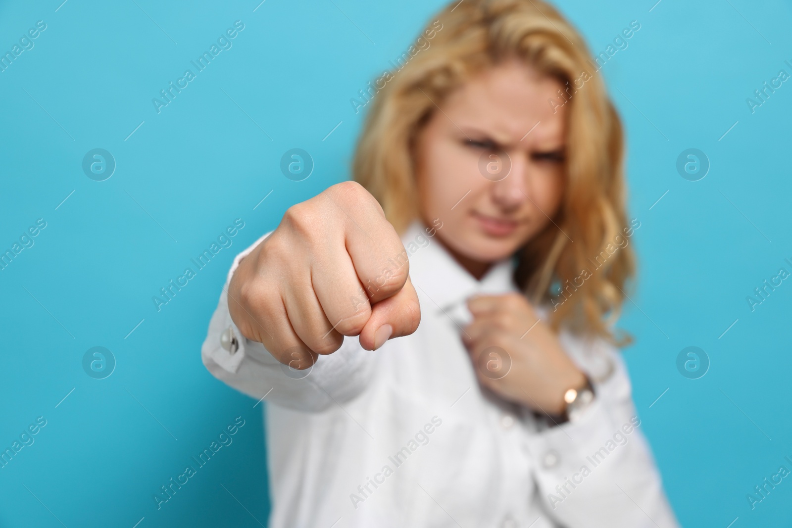 Photo of Young woman ready to fight against light blue background, focus on fist