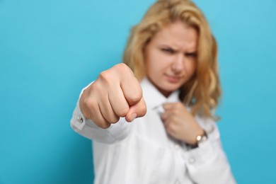Photo of Young woman ready to fight against light blue background, focus on fist