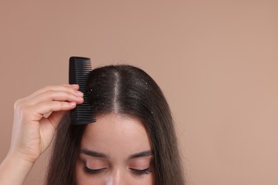 Woman with comb examining her hair and scalp on beige background, closeup with space for text. Dandruff problem