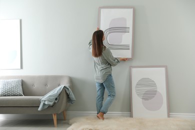Photo of Woman hanging picture on wall in room. Interior design