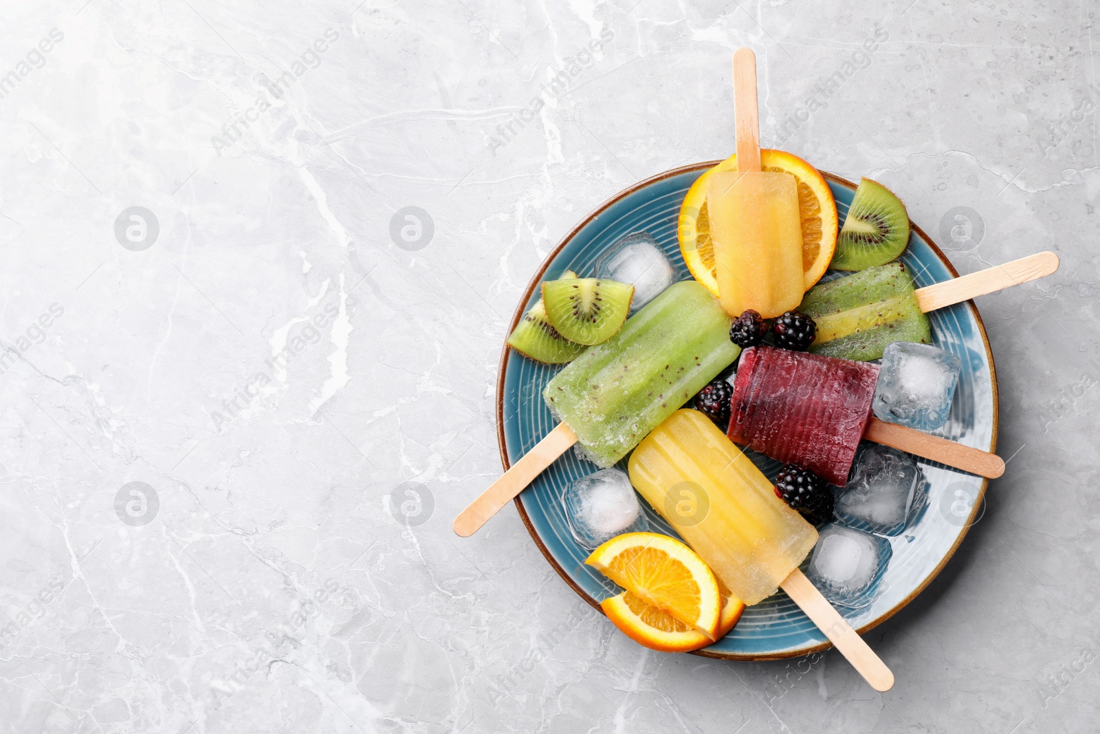 Photo of Plate of delicious popsicles, ice cubes and fresh fruits on light grey marble table, top view. Space for text