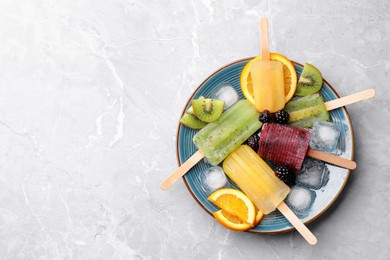 Plate of delicious popsicles, ice cubes and fresh fruits on light grey marble table, top view. Space for text