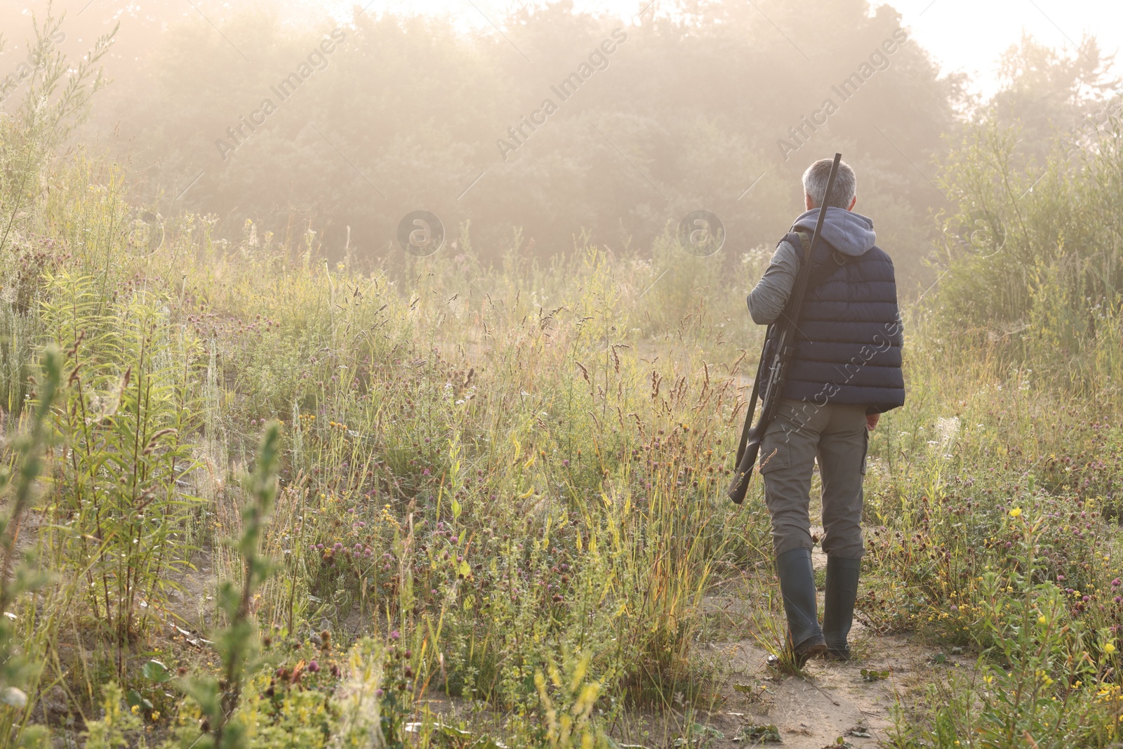 Photo of Man with hunting rifle outdoors, back view. Space for text