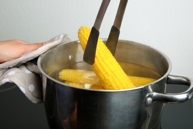 Photo of Young woman taking boiled corn cob from pot on stove, closeup