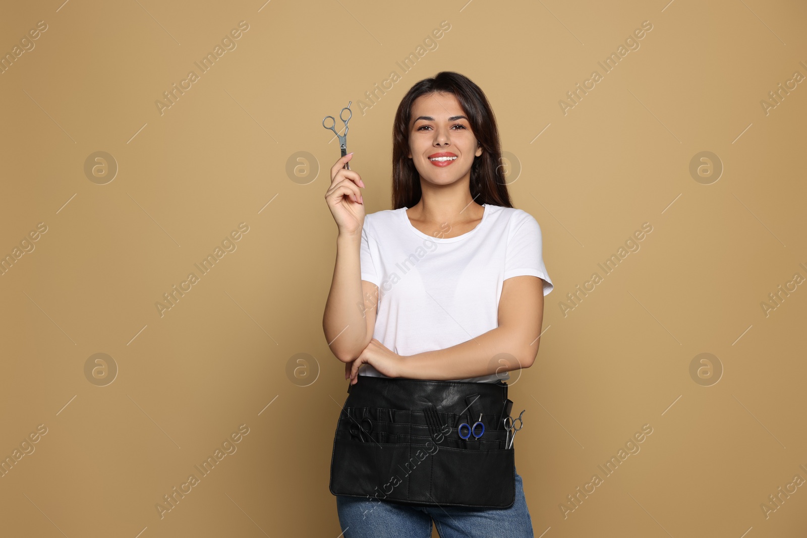 Photo of Portrait of happy hairdresser with professional scissors on pale orange background