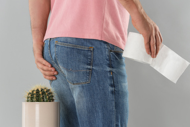 Photo of Man with toilet paper sitting down on cactus against light grey background, closeup. Hemorrhoid concept