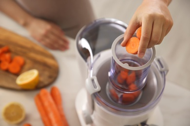 Photo of Young woman putting fresh slices of carrot into juicer at table in kitchen, above view
