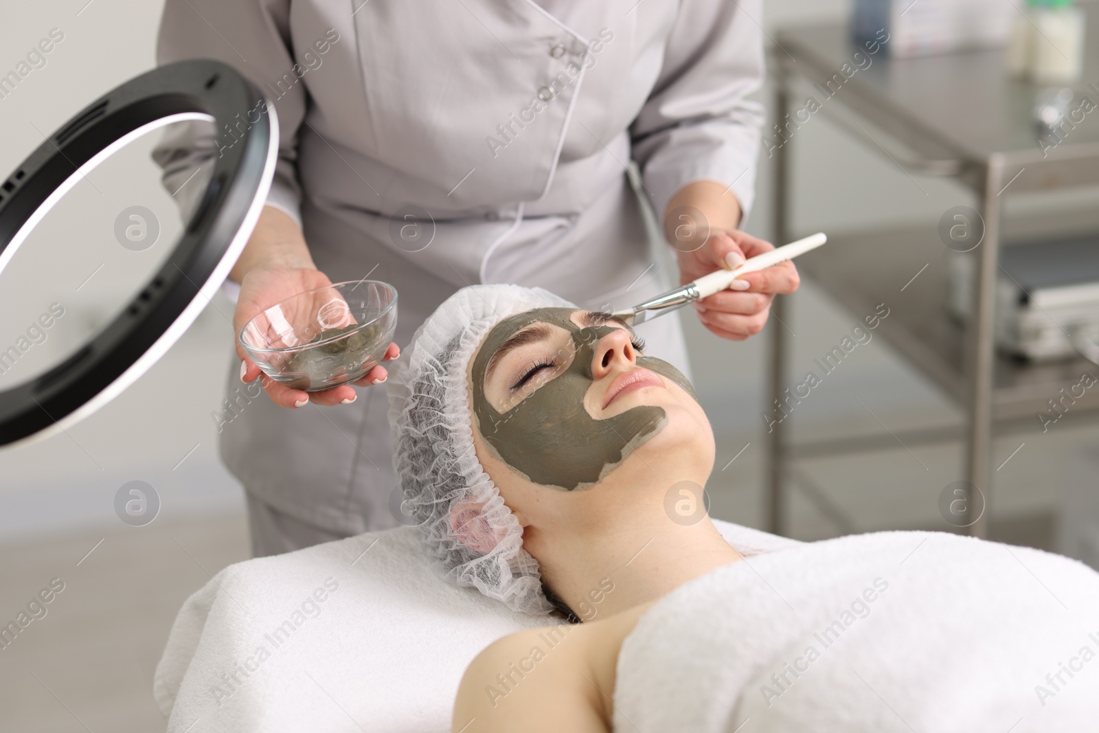 Photo of Cosmetologist applying mask on woman's face in clinic, closeup