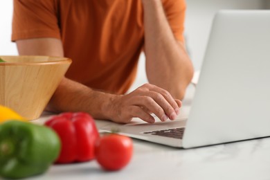 Photo of Man making dinner while watching online cooking course via laptop in kitchen, closeup