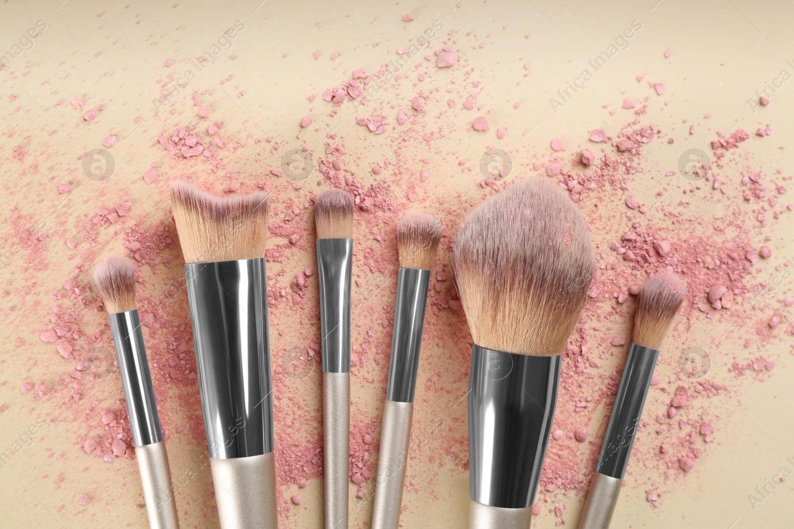 Photo of Makeup brushes and scattered eye shadow on beige background, flat lay