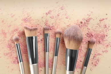 Makeup brushes and scattered eye shadow on beige background, flat lay