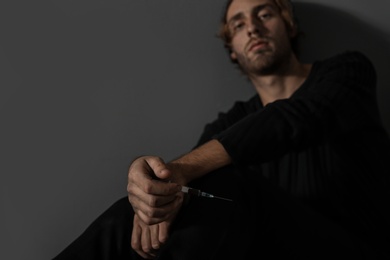 Photo of Young drug addict with syringe on grey background