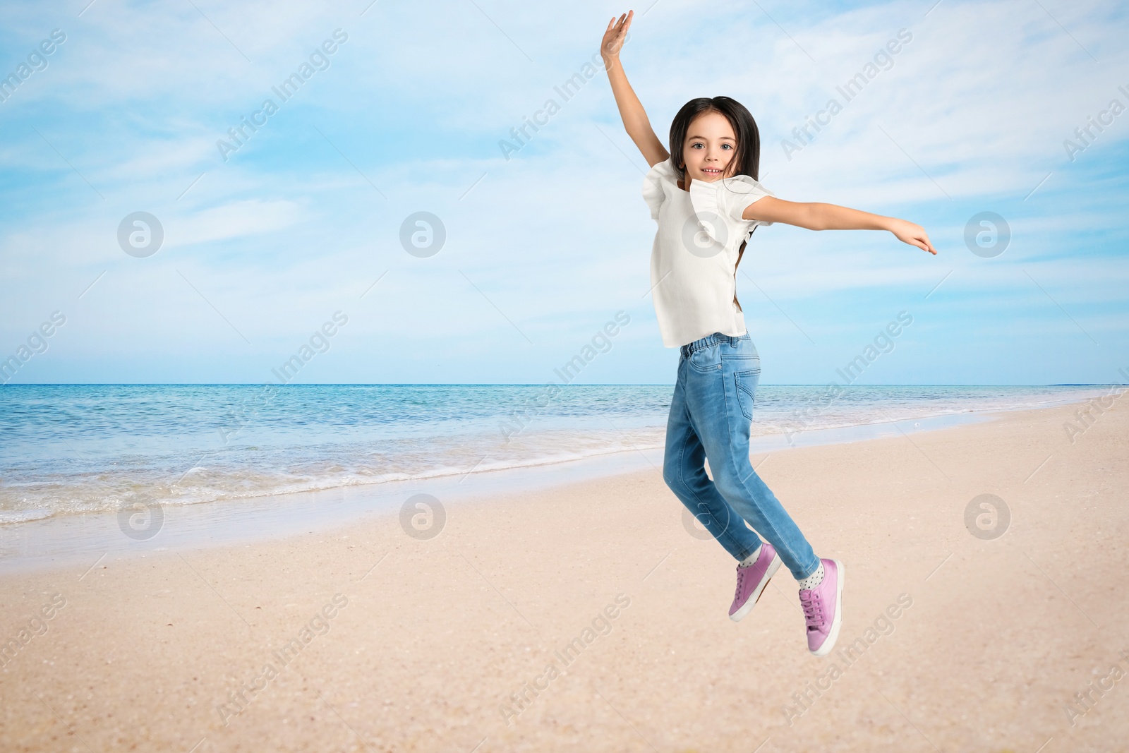 Image of Cute school girl jumping on beach near sea, space for text. Summer holidays