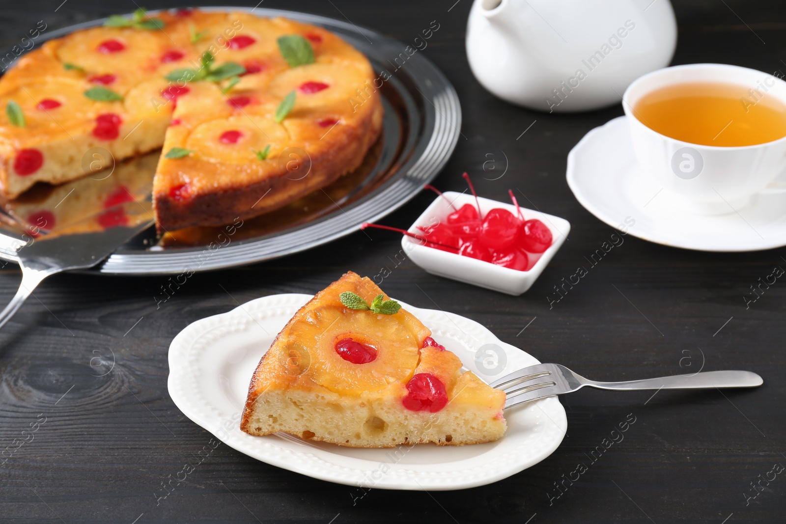 Photo of Piece of delicious pineapple pie with cherry and mint on black wooden table