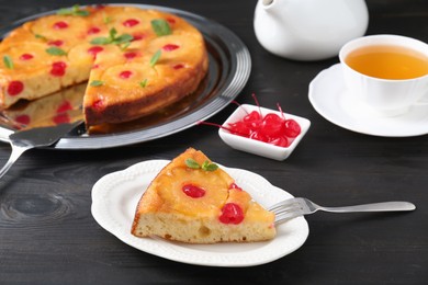 Photo of Piece of delicious pineapple pie with cherry and mint on black wooden table