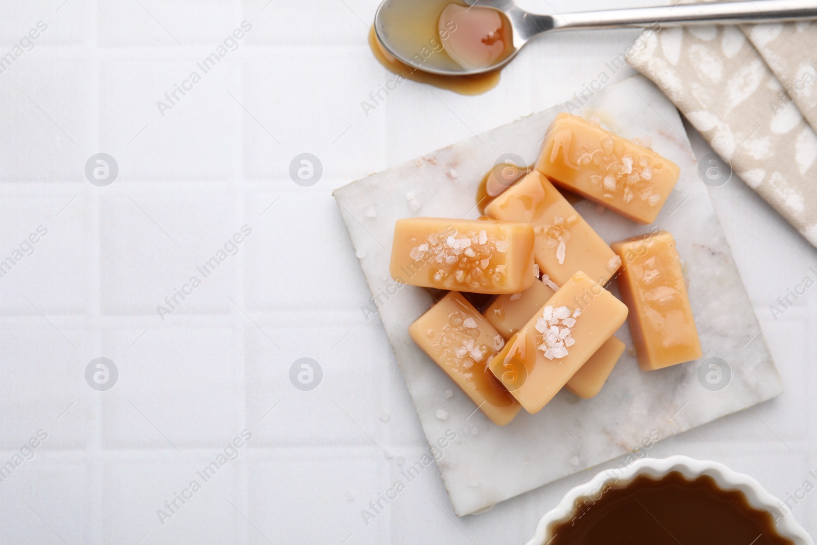 Photo of Delicious candies with sea salt and caramel sauce on white tiled table, flat lay. Space for text