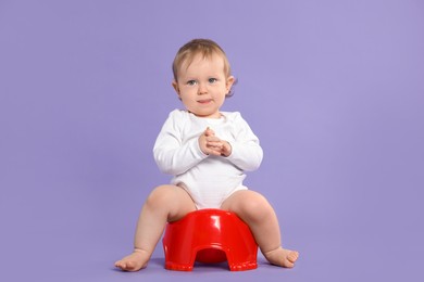 Little child sitting on baby potty against violet background