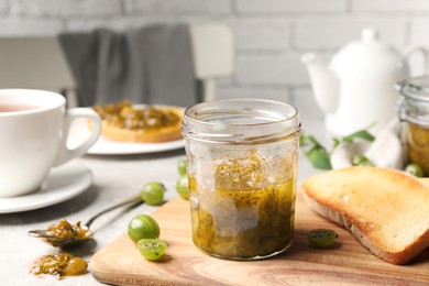 Photo of Jar of delicious gooseberry jam, toasts and fresh berries on table