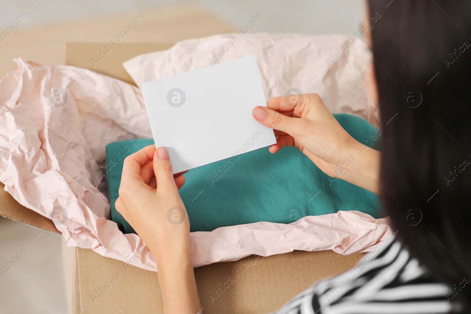 Photo of Young woman holding greeting card near parcel with Christmas gift at home