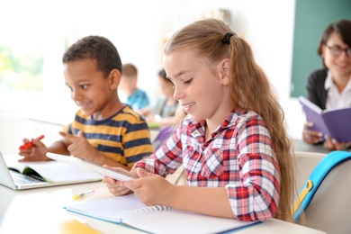 Photo of Cute little children with gadgets sitting at desk in classroom. Elementary school