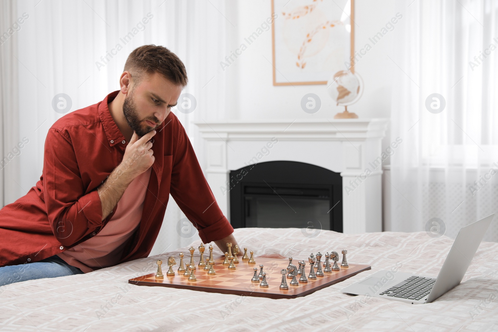 Photo of Thoughtful young man playing chess with partner through online video chat on bed at home