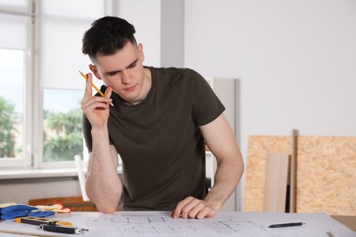 Photo of Young handyman working with blueprints at table in room
