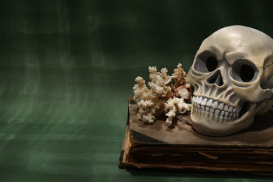 Photo of Human skull, old book and coral on dark green background. Space for text