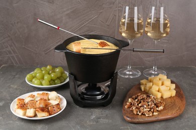 Photo of Fondue pot with tasty melted cheese, forks, wine and different snacks on grey table