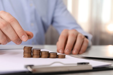 Man stacking coins at table indoors, closeup