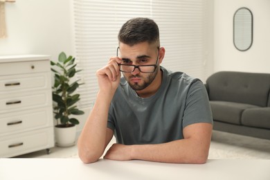 Photo of Sad man with glasses sitting at table indoors