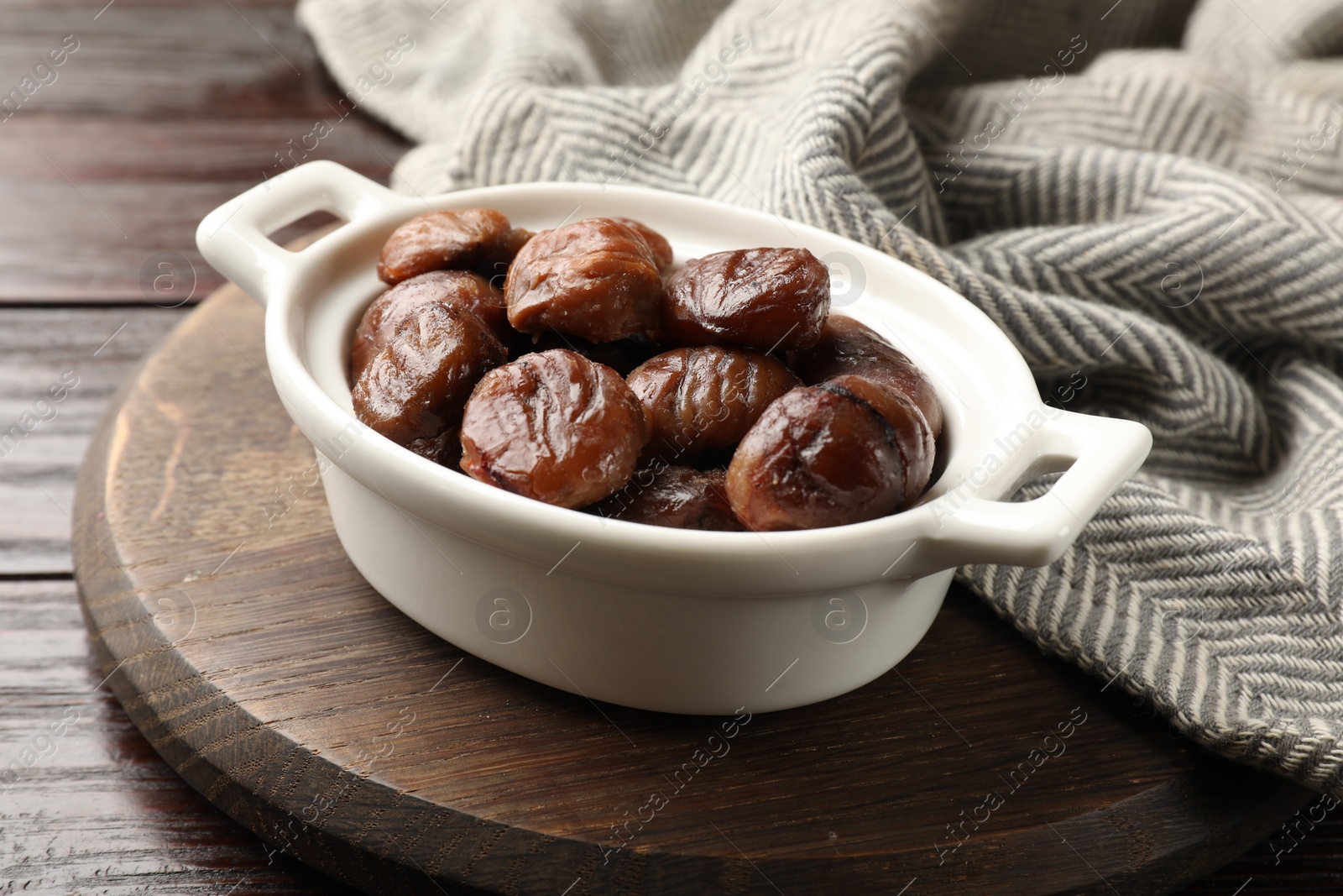 Photo of Roasted edible sweet chestnuts in dish on light wooden table